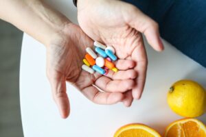 Mãos segurando cápsulas de suplementos ao lado de laranjas, simbolizando vitaminas e alimentação saudável