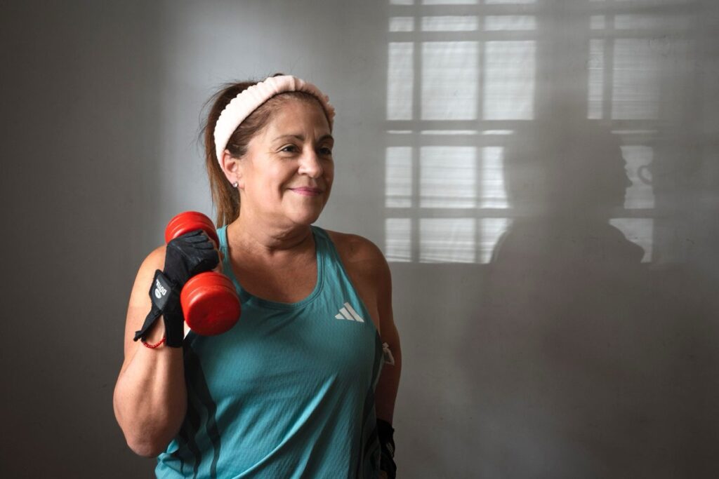Mulher madura sorrindo enquanto faz exercício com halter, ilustrando o treino de força para emagrecer depois dos 40